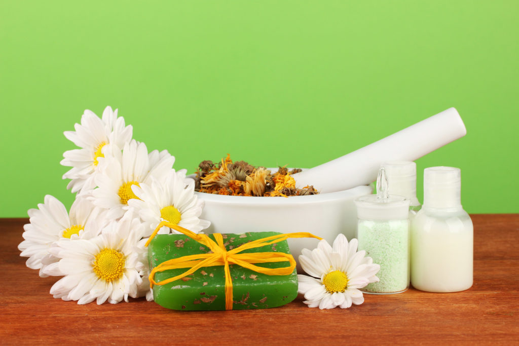 A soap tied with a bow, white flowers, white mortar and bottles with creams