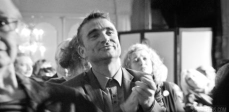 A black and white photograph of a man clapping. He is in a crowd of people