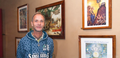 Alan Dronkers wearing a Sensi Seeds hoodie standing against a wall covered in framed paintings