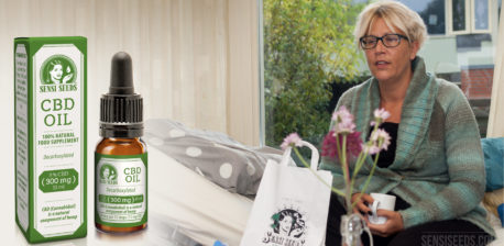 Woman sitting and holding a white cup and a pack of CBD oil beside