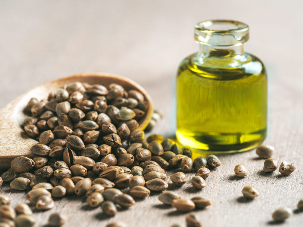 Spilled hempseeds from a wooden spoon and hempseed oil in a bottle