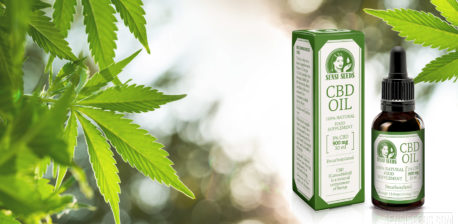 A CBD oil bottle next to its packaging. In the background are cannabis plants