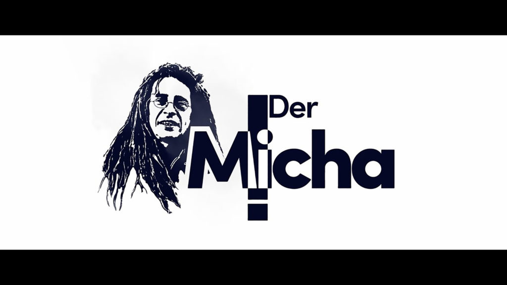 A white background with a mans face with glasses and dreadlocks next to the logo DerMicha