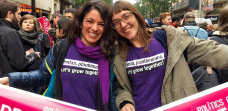 Two women in a crowd smiling and holding a pink banner