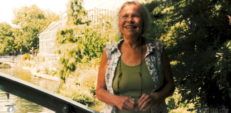 Photograph of cannabis legend Mila Jansen that was taken in the Amsterdam Botanical Gardens in 2018. Mila is wearing a green T-shirt and a blouse and is smiling at the camera.