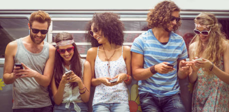 Three women and two men smiling and typing on their phones. They are all wearing sunglasses