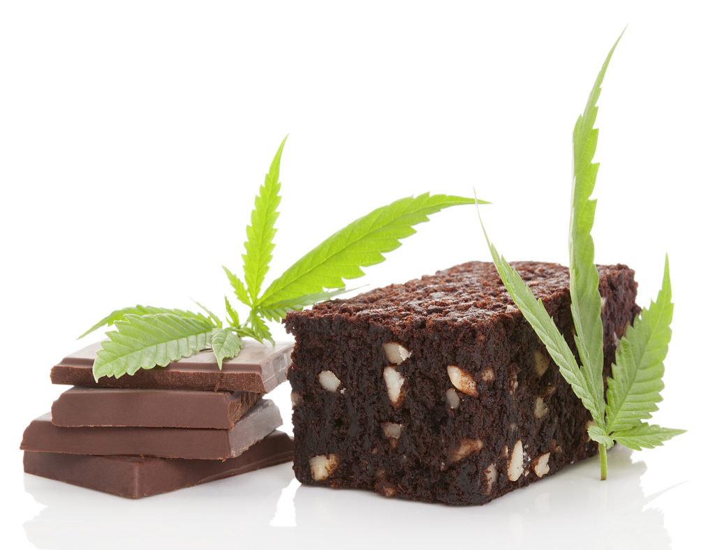 Een brownie en vier vierkanten van chocolade naast sommige cannabisbladeren