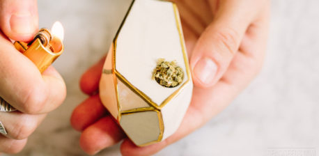 Een hand met een lichter in een witte en gouden cannabispijp