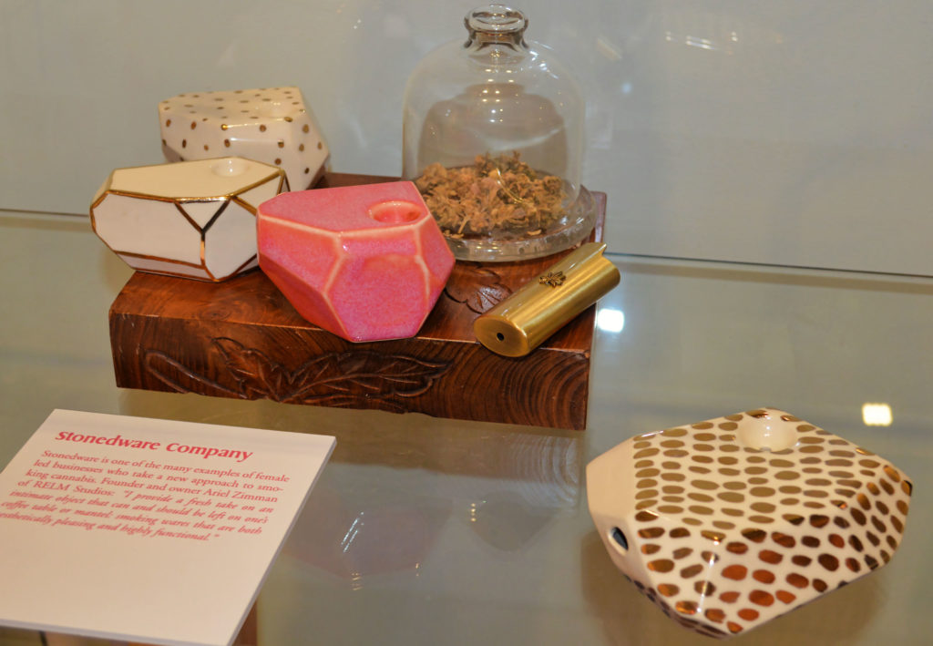 Four different cannabis pipes, a gold lighter, and a jar of cannabis displayed on a counter