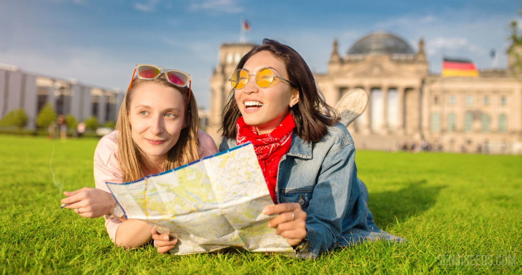 Dos chicas jóvenes que mienten en la hierba y que sostienen un mapa. Uno está sosteniendo una articulación