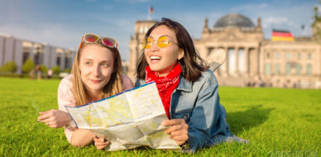 Two young girls lying on the grass and holding a map. One is holding a joint