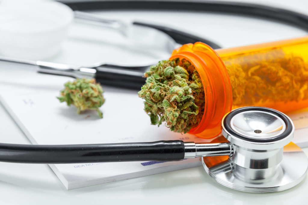 Primer plano de un bote color naranja que contiene cogollos medicinales de cannabis. A su lado, un fonendoscopio.