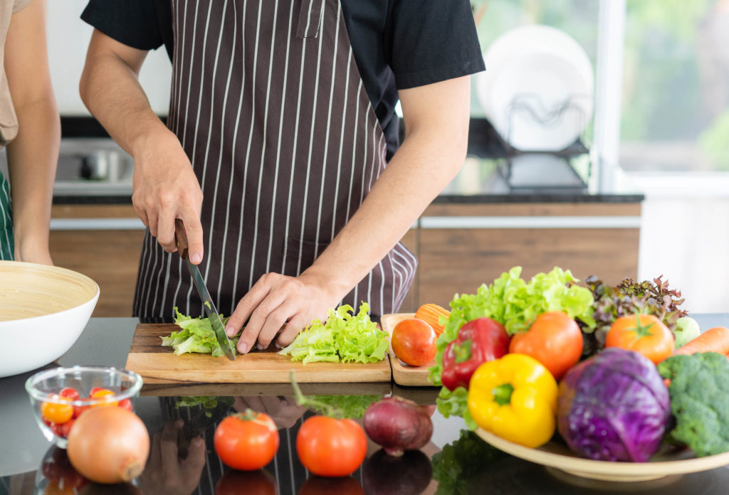 A person wearing an apron, chopping up lettuce and surrounded by vegetables