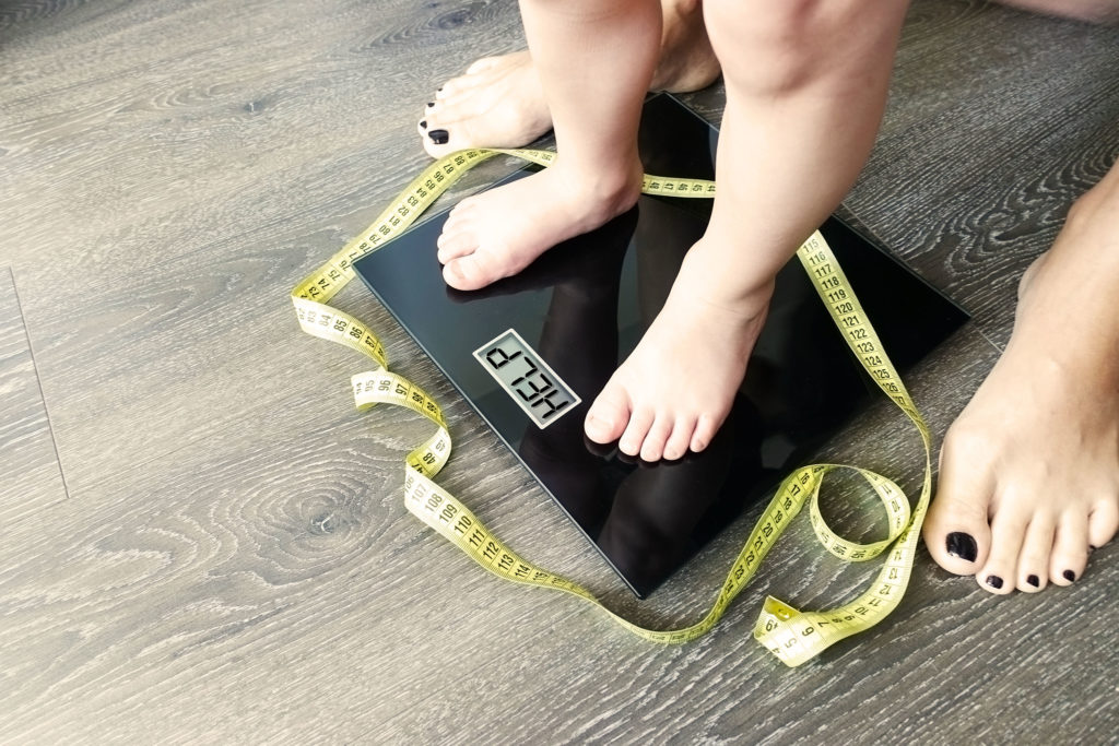 A child standing on weight scale and a woman standing behind him