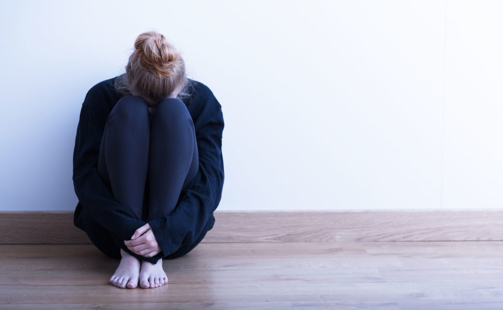 A woman sat with her head on her knees and arms around herself