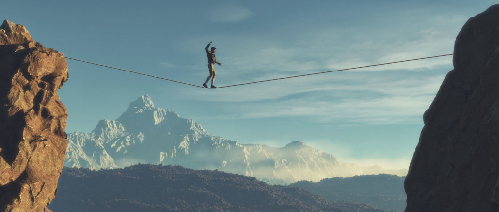 A person crossing a tightrope between two rocks with mountains in the background