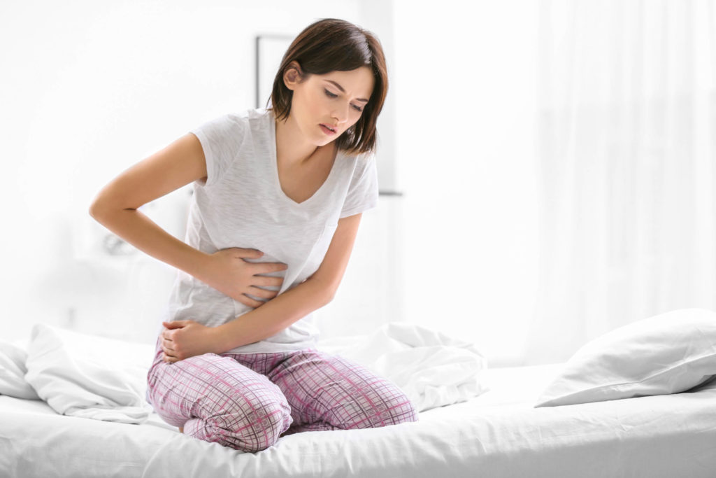 Une femme à genoux sur un lit avec des maux d'estomac