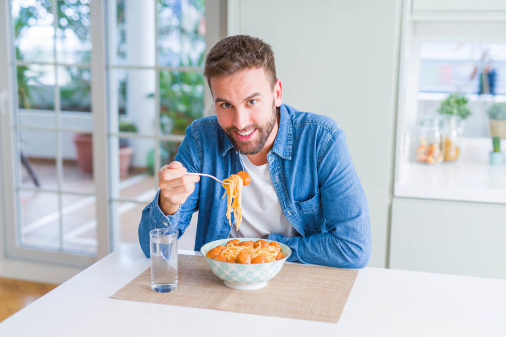 Un homme mangeant des nouilles avec une fourche à table