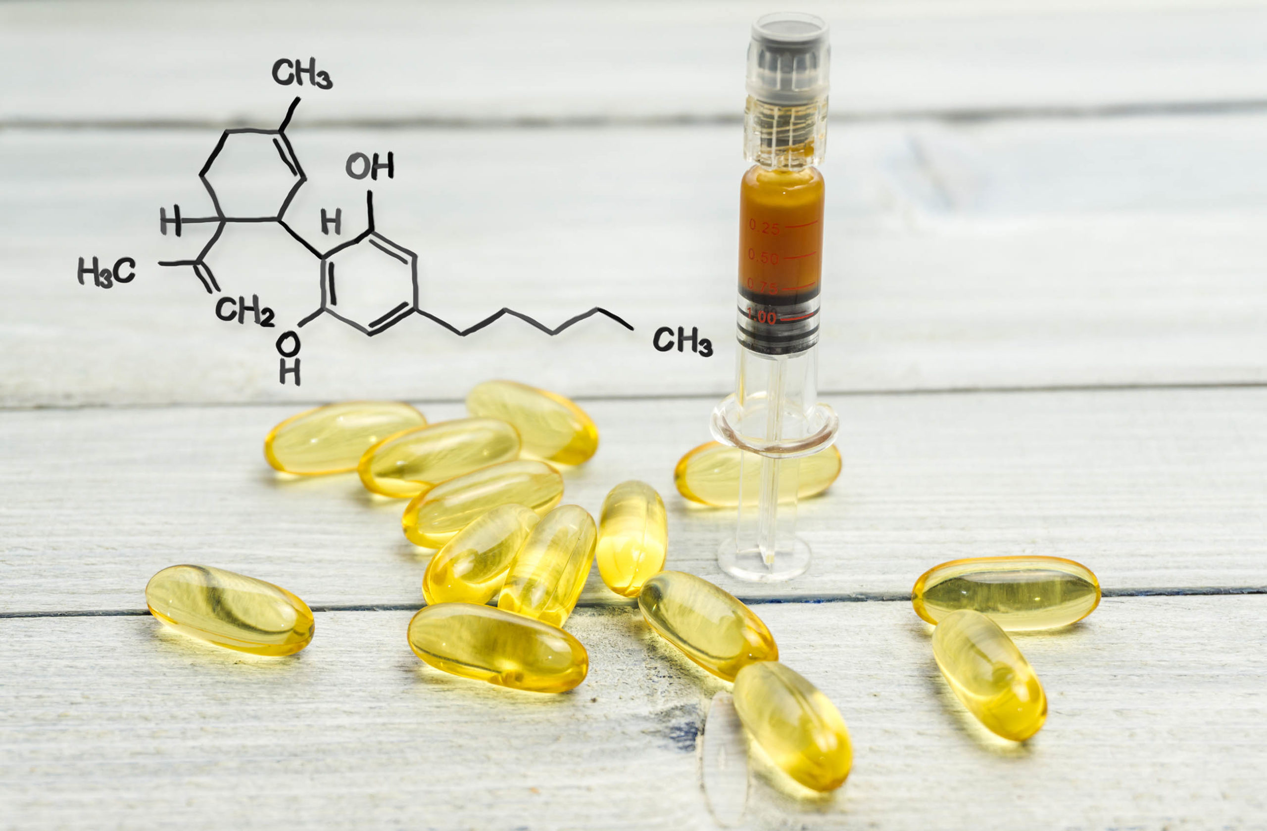 The chemical formula for CBD, yellow capsules and a syringe