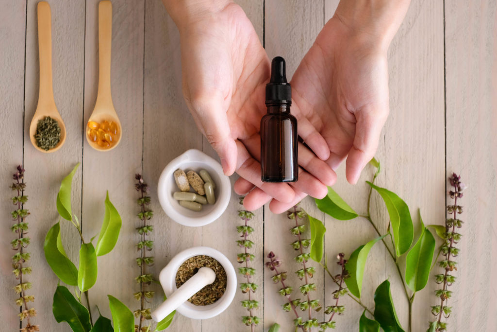 A person holding a glass bottle and two ramekins with different forms of CBD inside