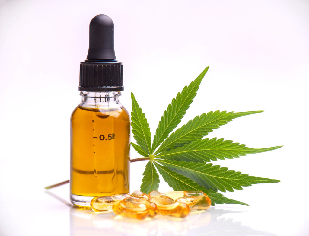 A CBD oil bottle and capsules and a cannabis leaf