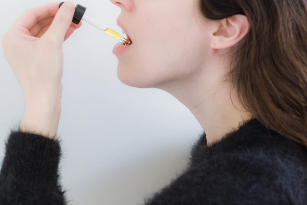 A woman using a pipette to dispense CBD oil in her mouth