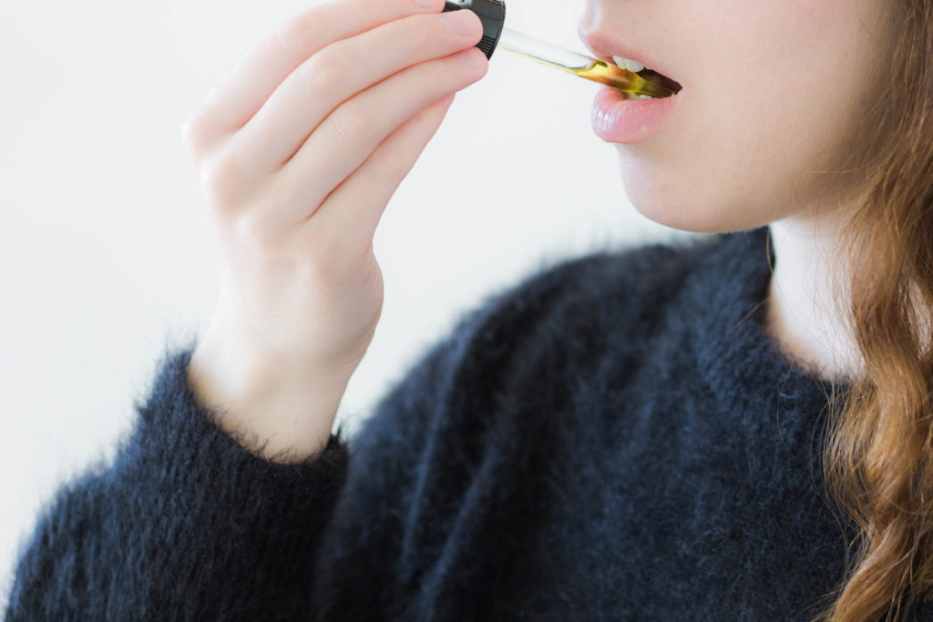 Eine Frau, die eine Pipette verwendet, um CBD-Öl in ihrem Mund zu verzichten