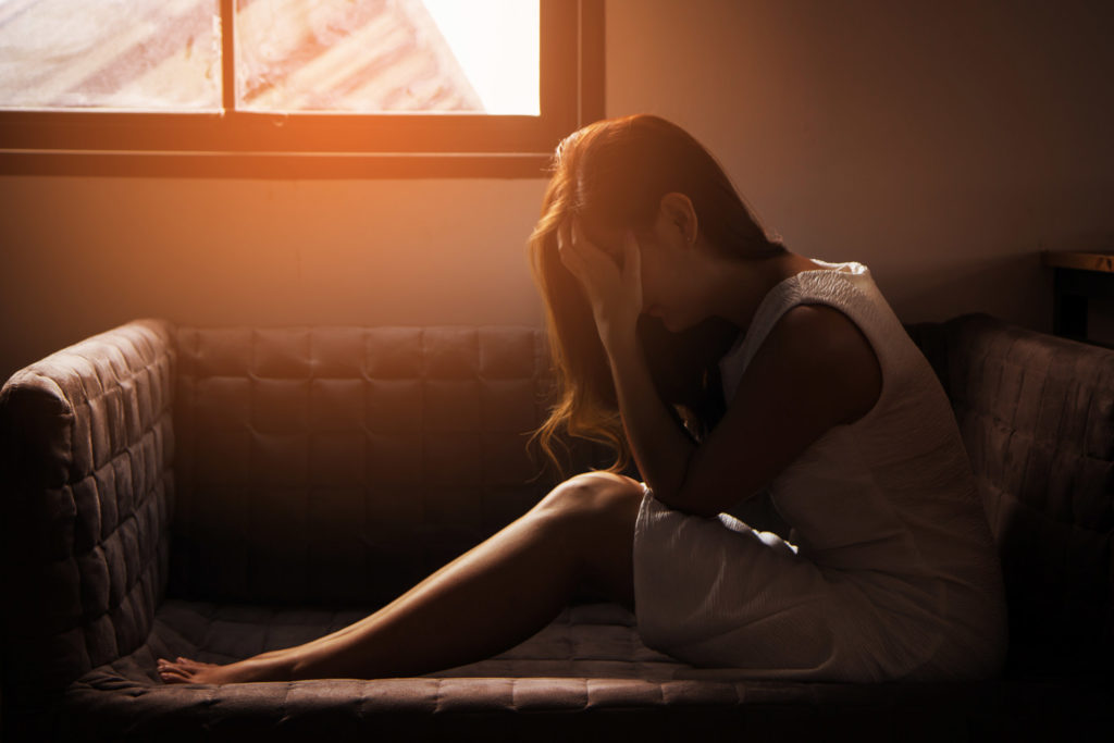 A brunet woman sitting on a sofa holding her aching head