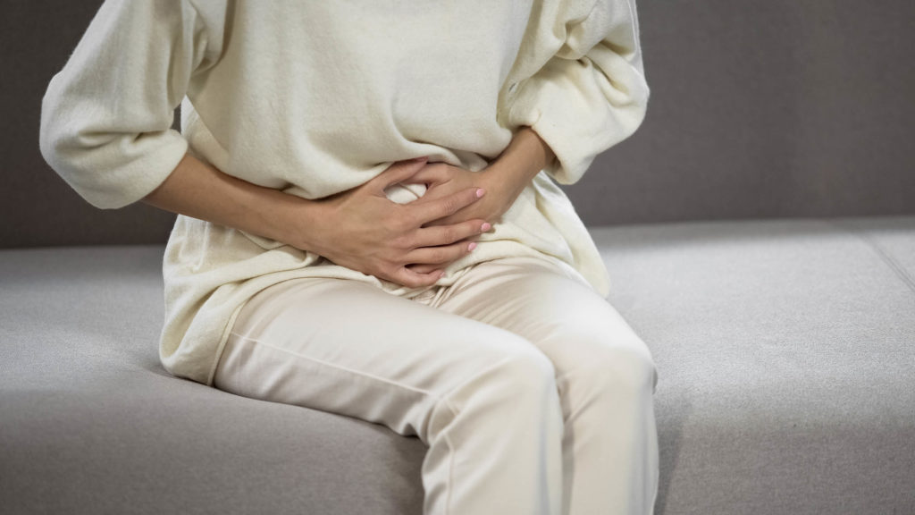 A woman dressed in white holding her aching stomach