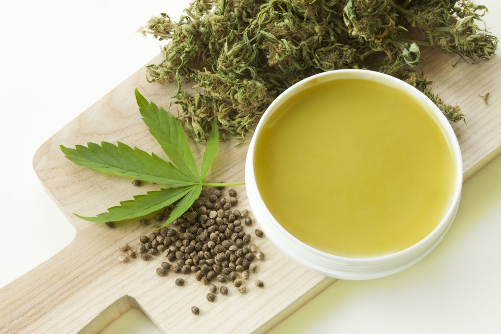 Three different forms of cannabis on a wooden board and ointment in a white pot