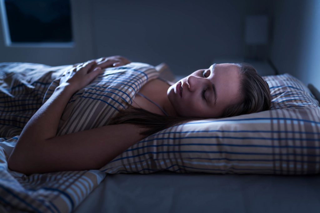 Una mujer durmiendo en una cama en una habitación oscura.