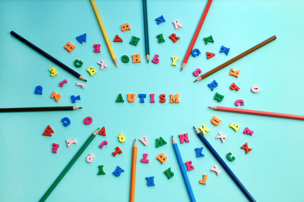 Different coloured pencils and letters arranged in a circle around the word "autism"