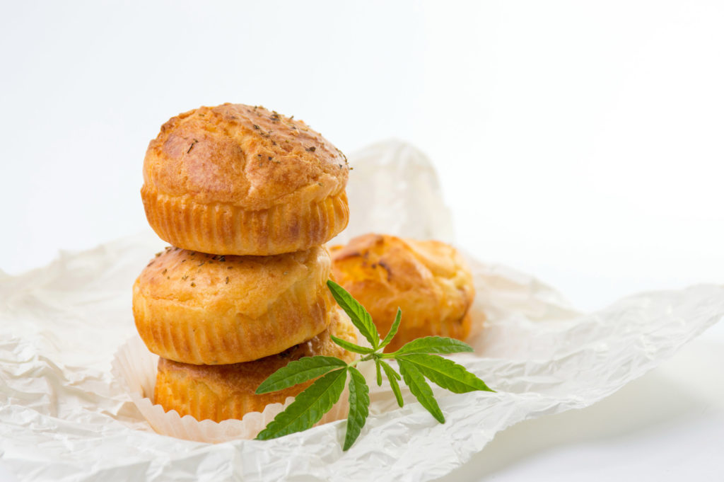 Cuatro pasteles de espacio marrón claro en una envoltura blanca con una hoja de cannabis a su lado.