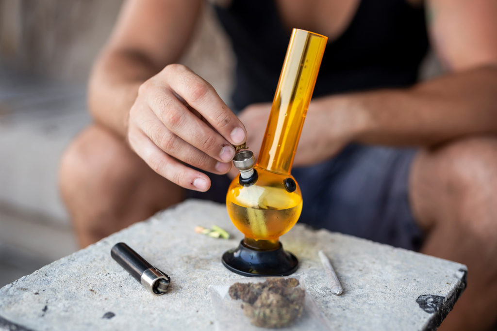 A person putting cannabis into a yellow bong