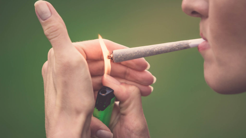 A woman lights a joint with a green lighter