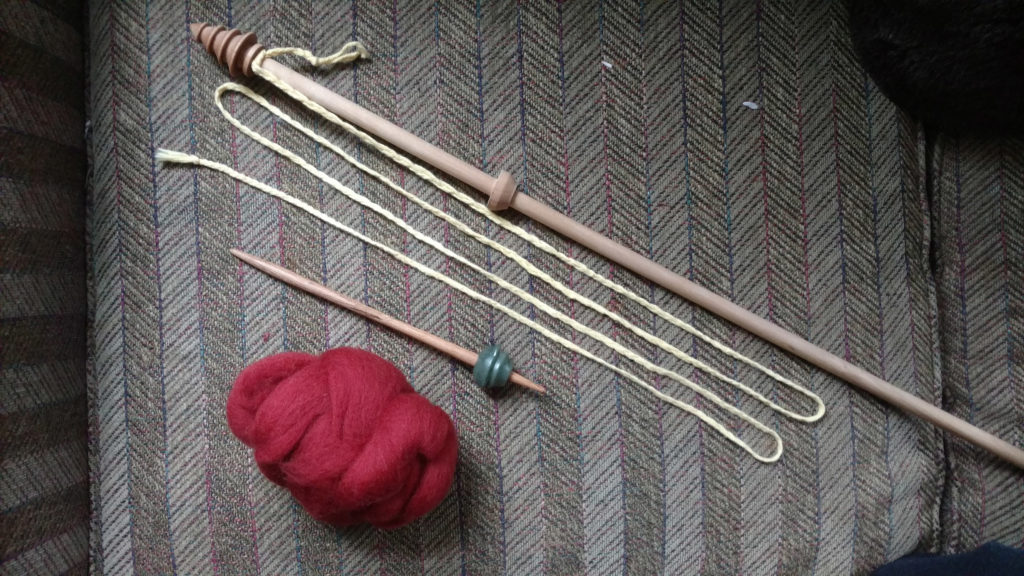 A distaff and a red yarn on a grey surface 