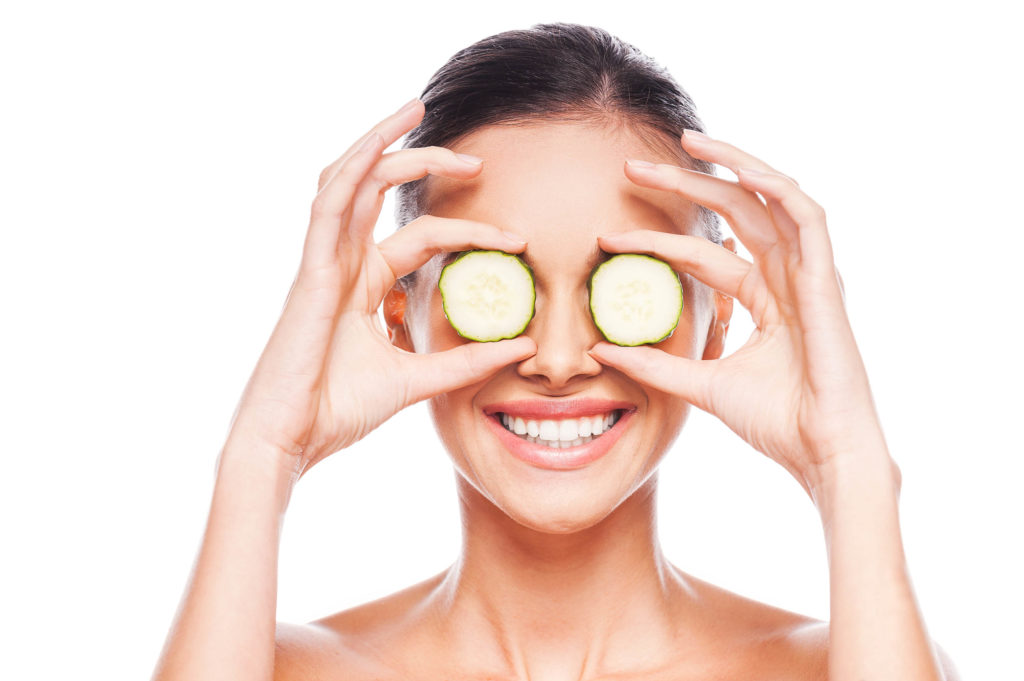 Woman holding cucumber slices in front of her eyes