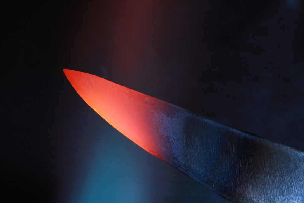 A black knife with a bright red tip that has been heated up