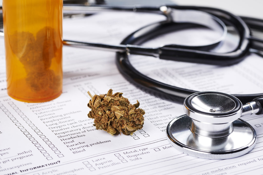 An orange tub of cannabis buds, a medical form, and a stethoscope