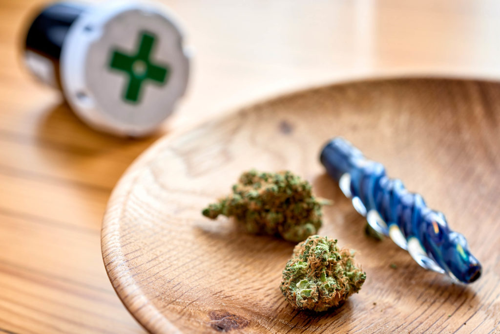 Two buds of cannabis in a wooden bowl, a medical jar and a pipe