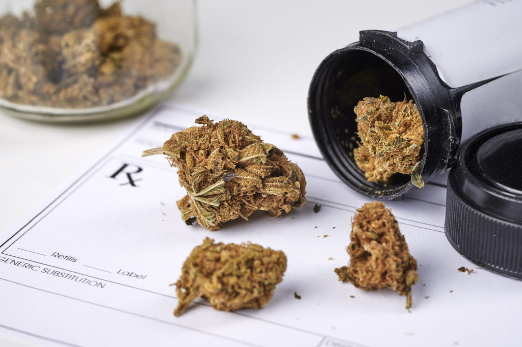 Loose cannabis buds on a piece of paper and a plastic container