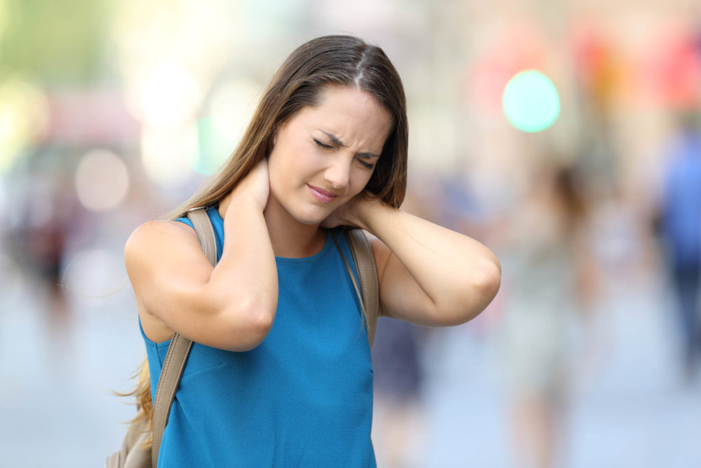 Una mujer con una expresión de dolor en su rostro, sosteniendo la parte posterior de su cuello.