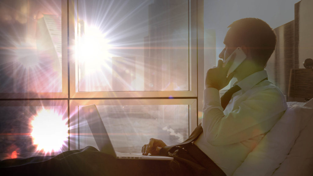 A man speaking on the mobile looking through the window with bright lights