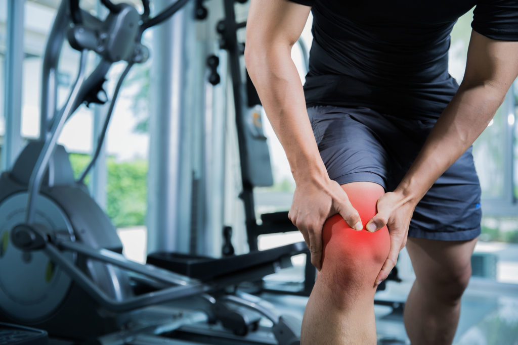 Een man in de sportschool die zijn knie houdt die hem pijn veroorzaakt