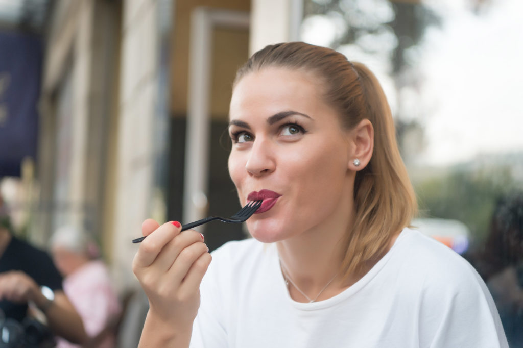 Une femme s'est assise dehors en souriant alors qu'elle aime manger la nourriture de sa fourchette en plastique noir