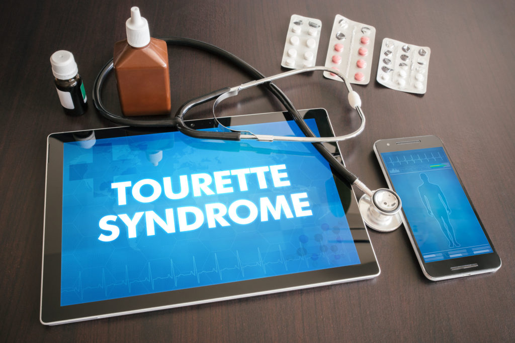 Un iPad qui affiche les mots "Syndrome de Tourette" à côté d'un iPhone, d'un stéthoscope et d'un médicament