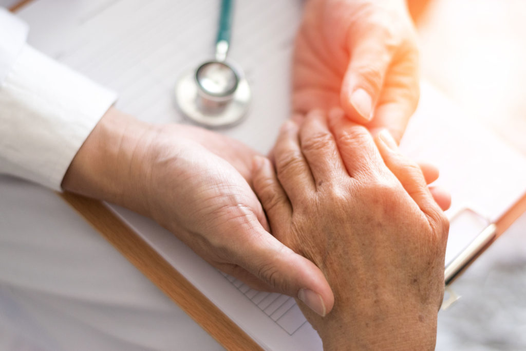 Un médecin tenant partiellement la main d'un patient de Parkinson au sommet d'un presse-papiers