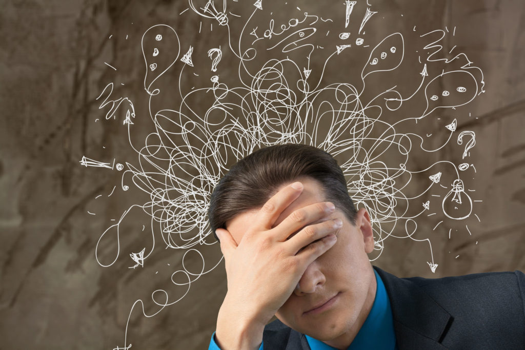 A man holding his forehead. Around his head are white scribbles and speech bubbles