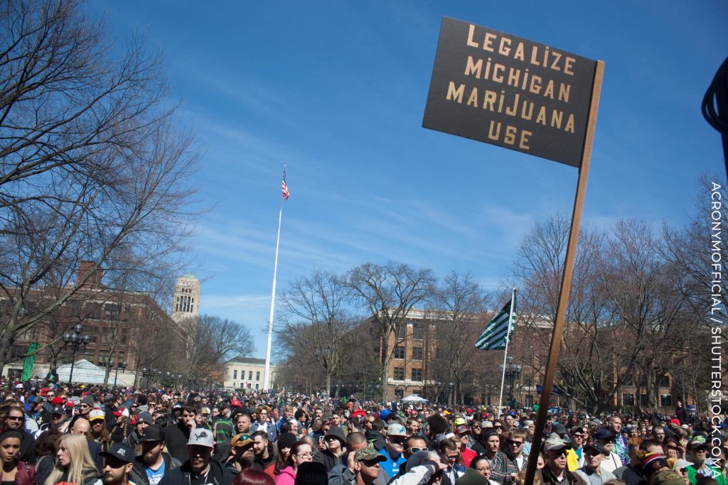 Una multitud en una protesta y un letrero con dice que 'Legalice Michigan Marijuana Uso'