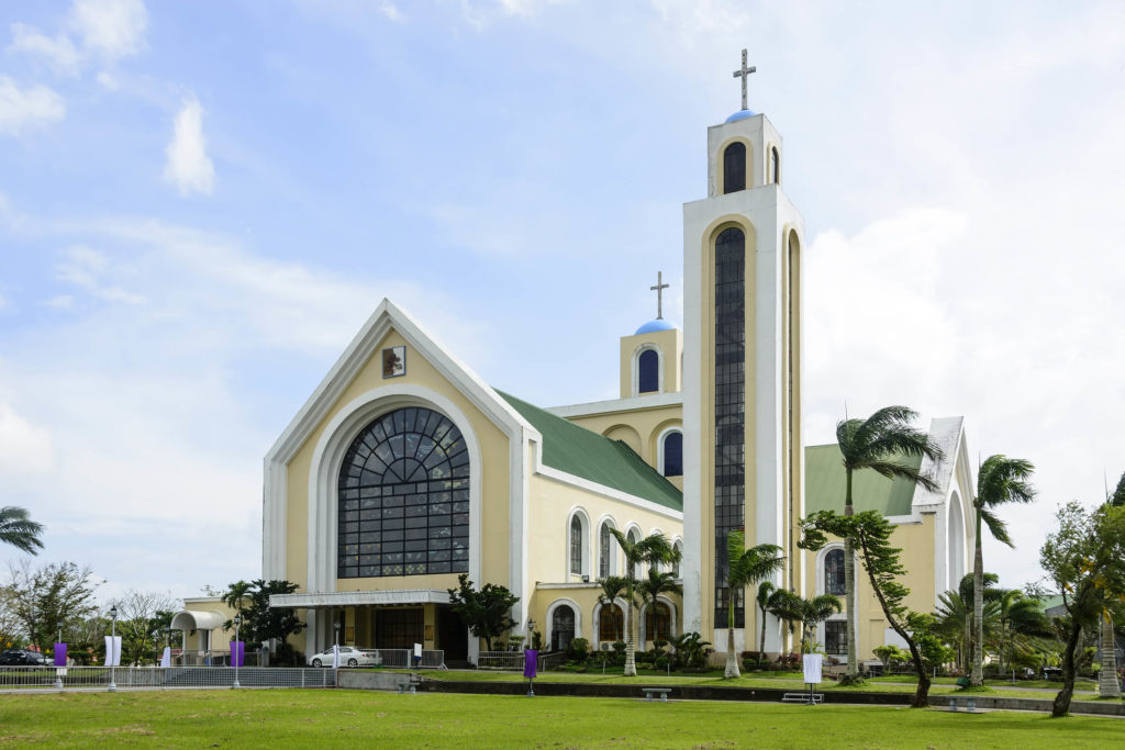 A yellow and green church building with palm trees surrounding it